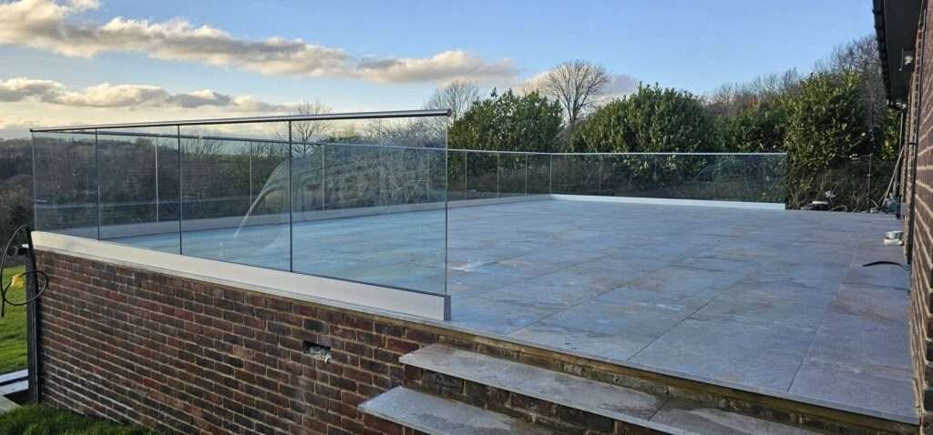 Frameless glass balustrade around a raised stone terrace